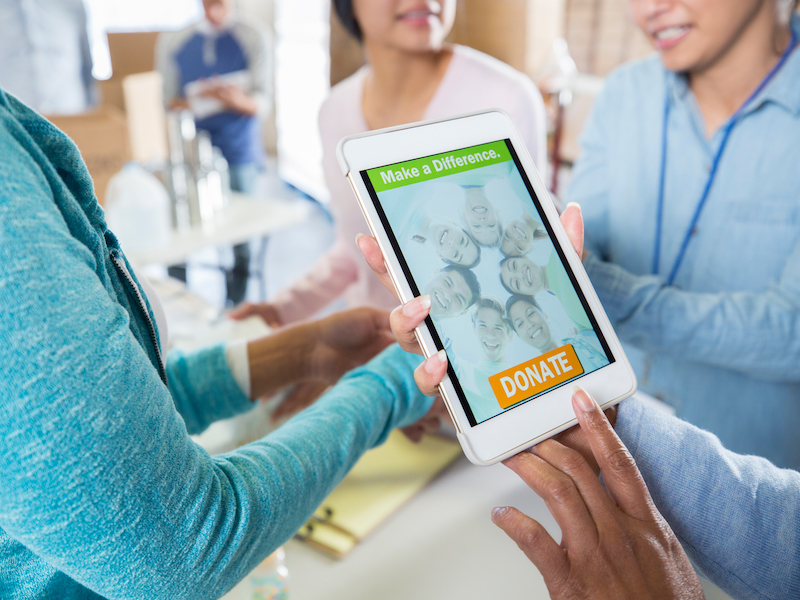 Group of unrecognizable women hold up "donate" advertisement on tablet