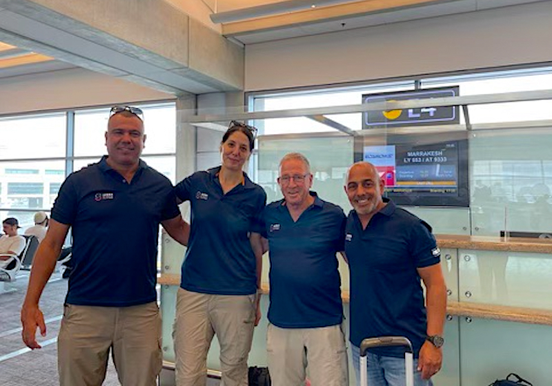 Three men and one woman wearing blue shirts with the emblem of the Humanitarian & Disaster Response Center (HDRC) team standing arm in arm in an airport terminal.