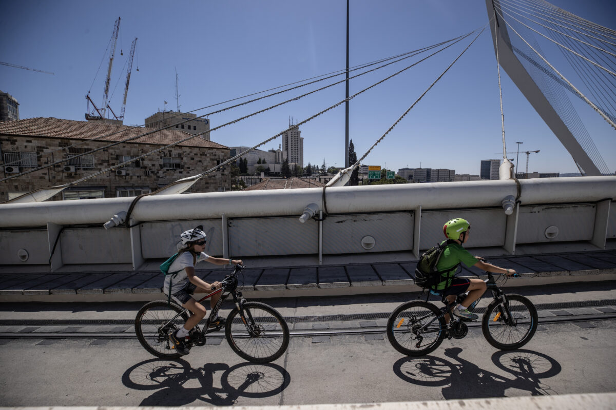 Israeli children ride their bikes on the light rail lines across the Chords Bridge at the entrance to Jerusalem on Yom Kippur on Monday.