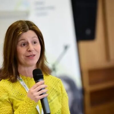 woman in yellow shirt speaks into a handheld microphone
